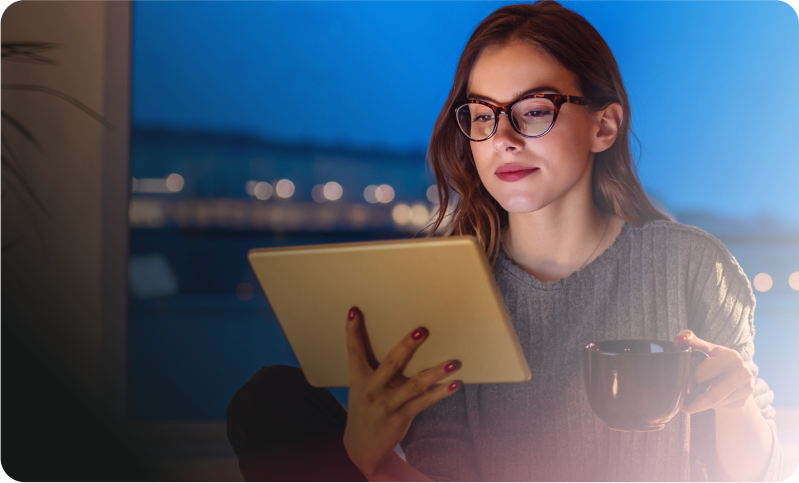imagem de uma mulher de óculos segurando uma xícara na mão esquerda, segurando um tablet com a mão direita e olhando fixamente para ele